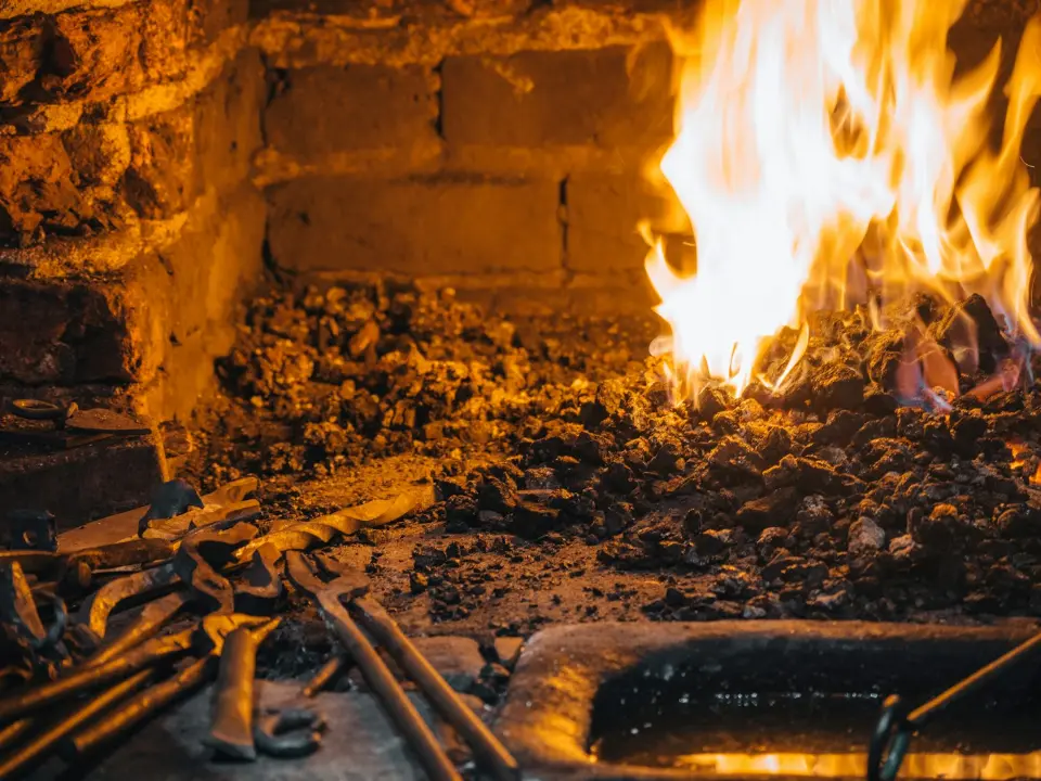 Foyer de forge en briques avec flammes, braises et outils de ferronnier posés devant