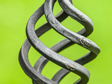 Barre de fer torsadée en spirale, terminée par une boule martelée, sur un fond vert flou