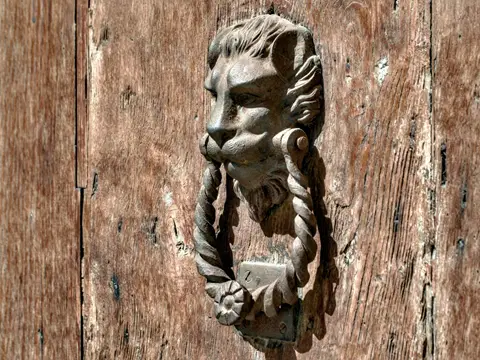 Heurtoir en métal patiné représentant une tête de lion tenant un anneau torsadé, sur une vieille porte en bois