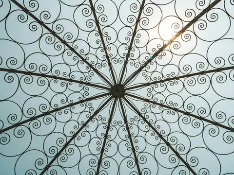 Voûte en fer forgé couverte de volutes qui rayonnent depuis un centre, vue d'en dessous sur un ciel clair
