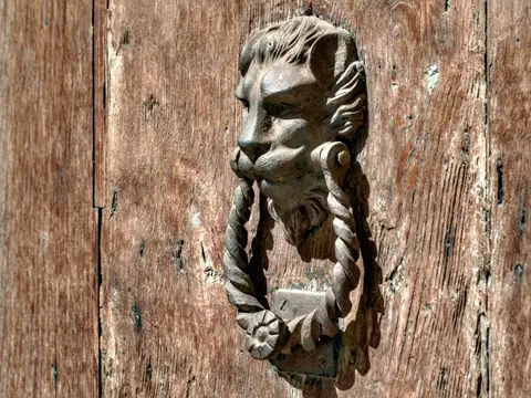 Heurtoir en métal patiné représentant une tête de lion tenant un anneau torsadé, sur une vieille porte en bois
