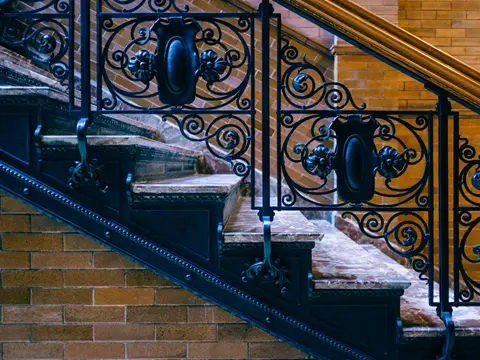 Rampe d'escalier en fer forgé noir à volutes et médaillons, marches de marbre, mur de briques et main courante en bois