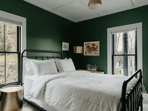 Lit en fer forgé noir dans une chambre aux murs vert profond, avec un lampadaire et une table d'appoint en laiton