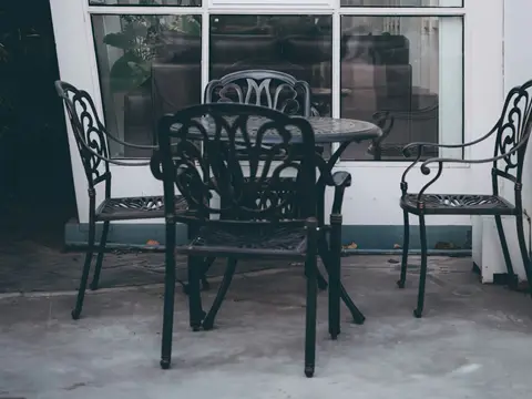Table ronde et trois fauteuils en fonte noire à dossiers ouvragés, devant une grande baie vitrée à petits carreaux, ambiance douce