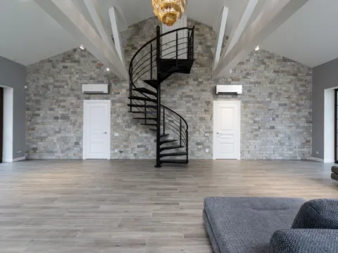 Escalier colimaçon en acier noir dans un grand séjour au mur de pierre