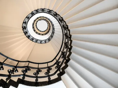 Vue plongeante sur un colimaçon à rampe en fer forgé noir orné de volutes