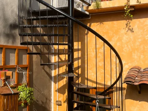 Escalier colimaçon en acier noir sur une façade ocre dans une cour ensoleillée