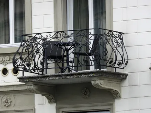 Balcon en fer forgé noir à volutes, table et deux chaises, façade claire