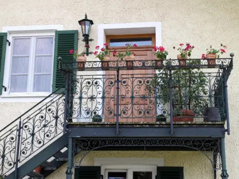 Balcon et escalier extérieur à rampe en fer forgé noir à volutes sur une façade crépie claire