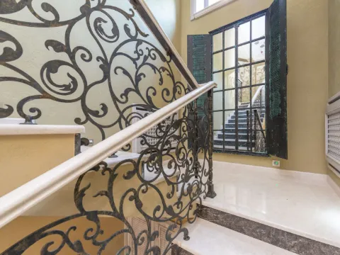 Rampe d'escalier en fer forgé à grandes volutes de teinte bronze, main courante de marbre clair