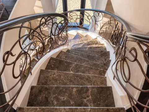 Escalier en spirale vu de dessus, rampes en fer forgé ouvragé de teinte bronze et marches de marbre brun