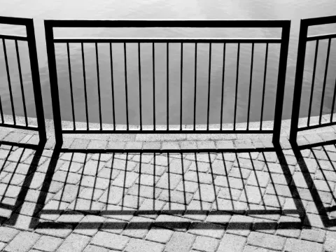 Garde-corps barreaudé en acier noir projetant ses ombres sur un sol pavé, vue en noir et blanc