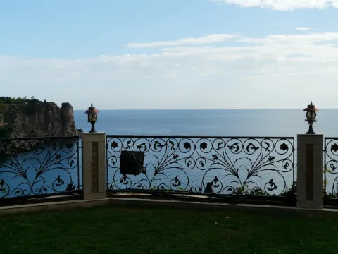 Terrasse de villa face à la mer bordée de panneaux en fer forgé à volutes entre des piliers de pierre