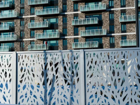 Panneaux de métal blanc découpés de motifs végétaux formant claustra devant un immeuble moderne