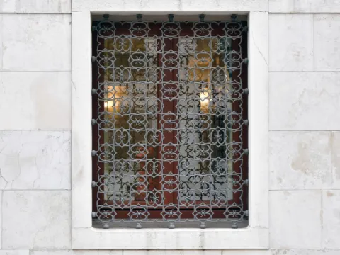 Fenêtre encadrée de marbre blanc fermée par une grille en fer forgé à enroulements serrés