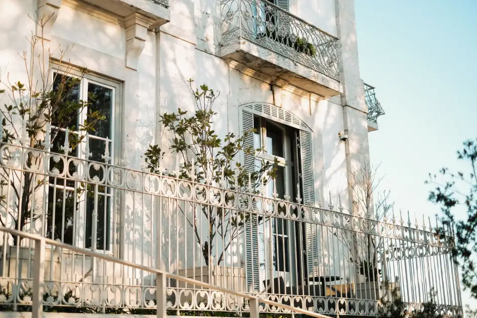 Clôture en fer forgé blanc ouvragé devant une façade claire à la lumière du soir