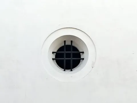 Ouverture ronde dans un mur blanc lisse, fermée par une grille de barreaux noirs