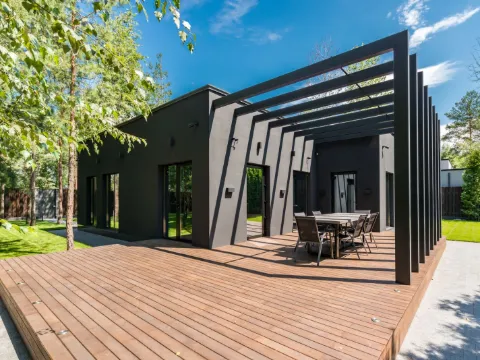 Portiques noirs fins en enfilade au-dessus d'une table de terrasse devant une maison contemporaine sombre