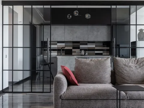 Salon gris et verrière à carreaux noirs laissant voir la cuisine ouverte
