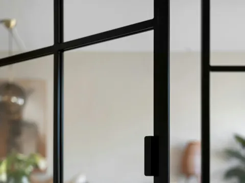 Détail d'une porte vitrée à carreaux d'acier noir avec poignée, salle à manger floue derrière